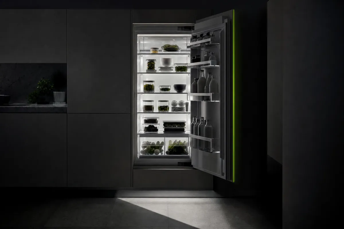 Una nevera abierta en una cocina a oscuras, con los estantes ordenados iluminados por la luz interior.